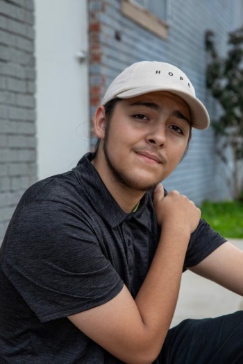 High school drop-outs: Headshot of young man with long dark hair pulled back in light baseball cap, black shirt