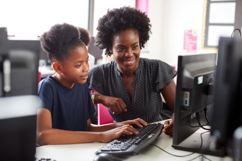 Black teachers leaving Philadelphia: Black woman in gray top sits t computer monitor next to young Black girl in black top typing on keyboard