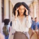 Black teachers leaving Philadelphia: Black woman in white blouse and tan skirt standing in hallway full of children holding head in her hands with eyes closed and grimacing face