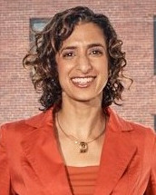 College listening cohort: Headshot woman with bobbed light brown hair in orange top with greenery in background