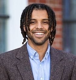 College listening cohort: Headshot Black man with medium dreds in brown tween suit with light blue shirt