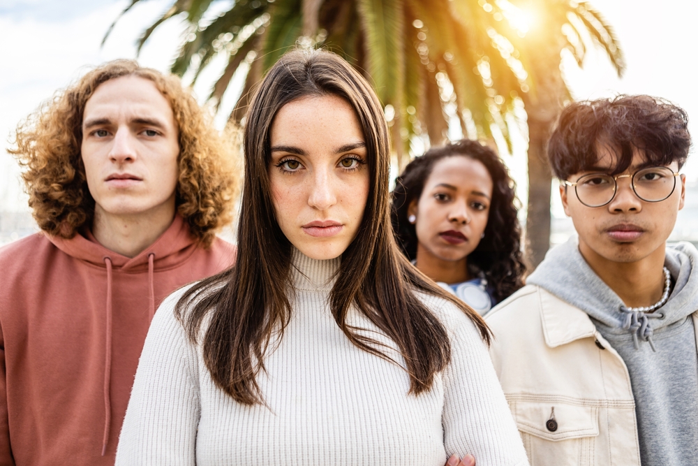 High school drop-outs: Close-up of four mixed ethnicity young adults - 2 women and two men - stare into camera with serious faces.