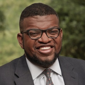 Immigration & scools: Headshot mature Black man with short blach hair and glasses in brown suit and tie with white shirt