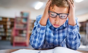 Math tests takeaways: Young boy sits with head in hands at white desk