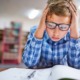 Math tests takeaways: Young boy sits with head in hands at white desk