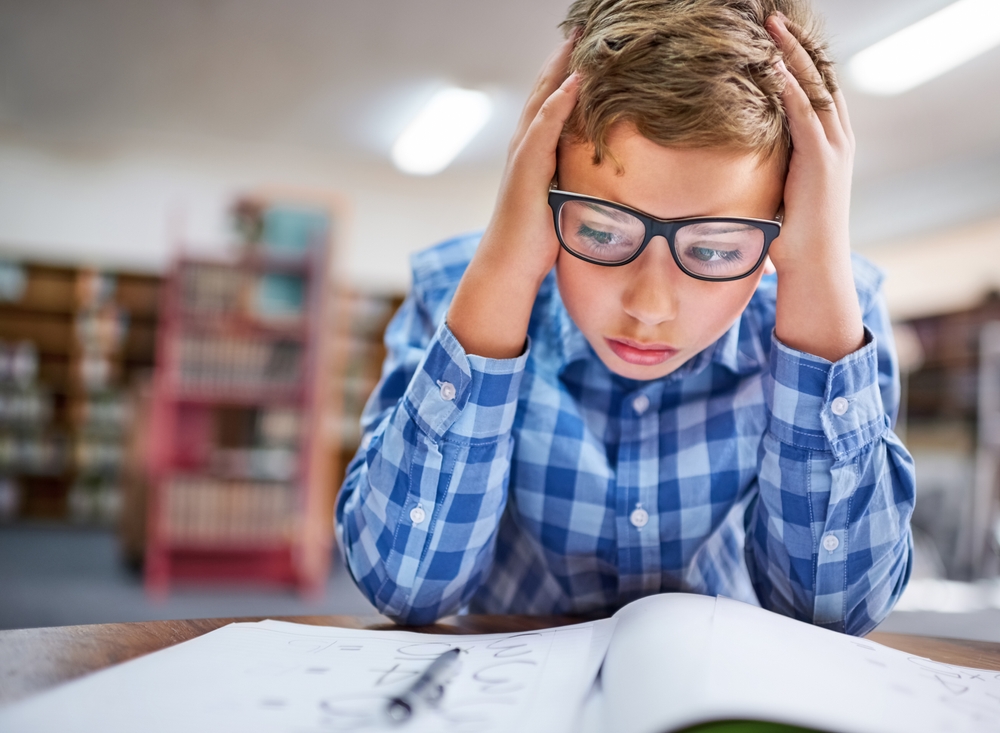 Math tests takeaways: Young boy sits with head in hands at white desk