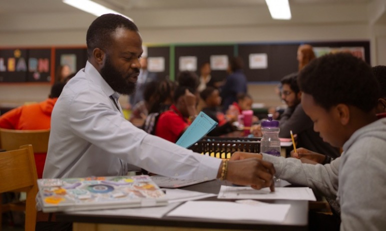 Maryland push to scale up high dosage math tutoring: black male tutor pointing at paper while helping student at table