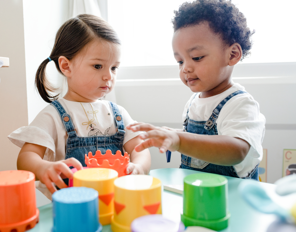 Childcare like Hunger Games: 2 toddlers play with toys on a low table