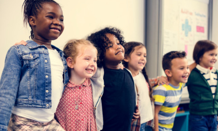 Childcare: several young children stand in a line with arms around each others shoulders