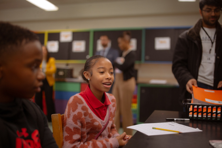 Maryland push to scale up high dosage math tutoring: Black teen with black air pulled back in red print sweater sits at classroom desk