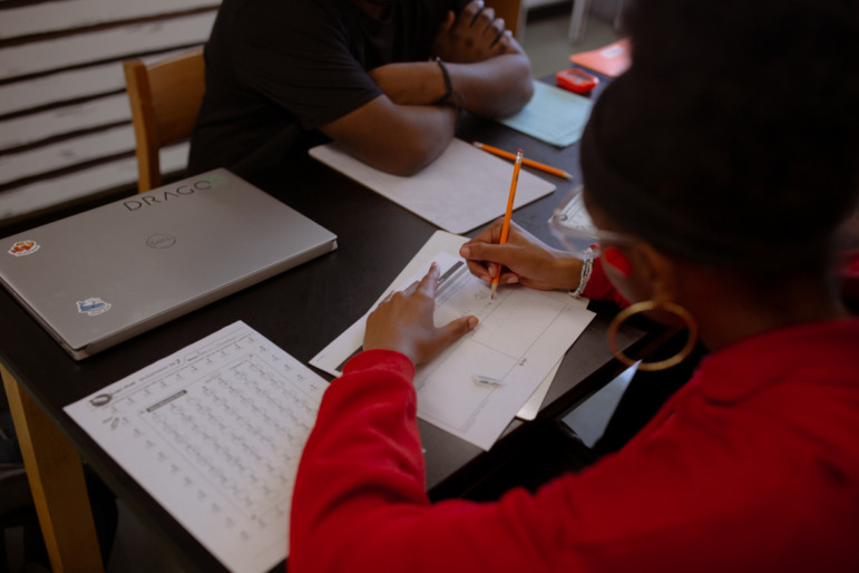 Maryland push to scale up high dosage math tutoring: Black girl in red sweater sits at desk across from anotheer Black student filling out paper