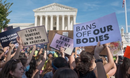 Abortion bans cause population migration: Several people with abortion-related and-painted protest signs stand outside in large group