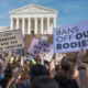 Abortion bans cause population migration: Several people with abortion-related and-painted protest signs stand outside in large group