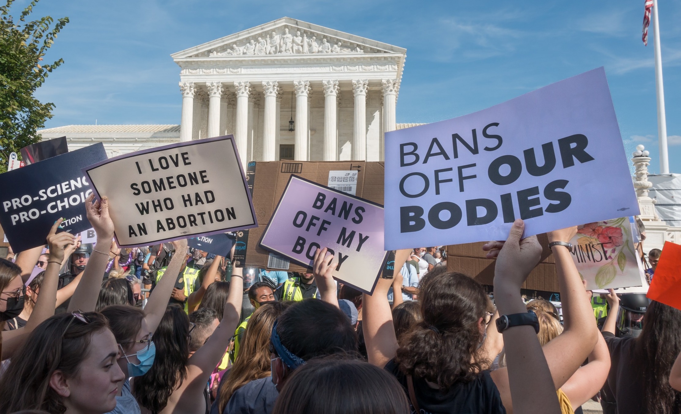 Abortion bans cause population migration: Several people with abortion-related and-painted protest signs stand outside in large group