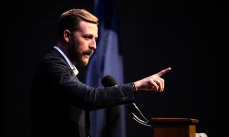 Oklahoma check students' parents document: Man with short brown hair in navy suit stands speaking at podium while gesturing with pointing right hand