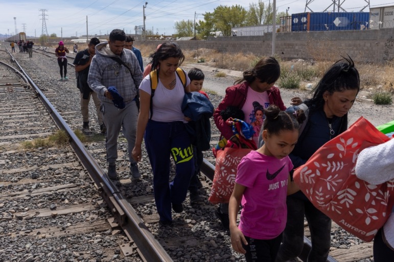 Oklahoma check students' parents document: Several aduts and young children most carrying sacks or wearing backpacks, walk along railroad tracks