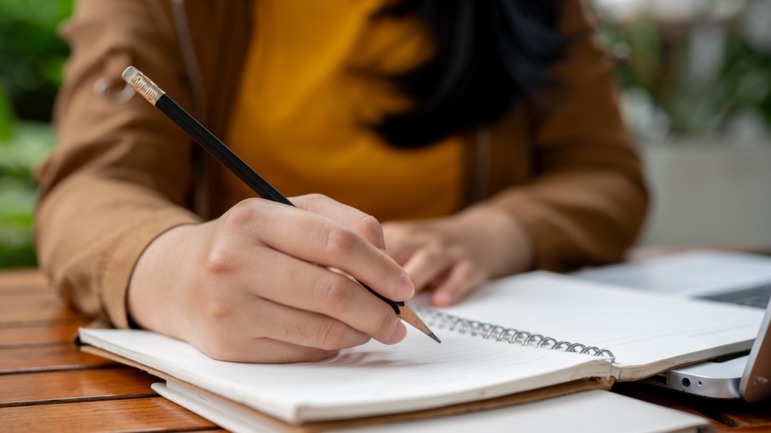 Handwriting versus keyboard: Close-up image of adults hands and arms writing with a pen on paper in wire-bound notebook