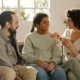 Parenting challenged kids: Two dark-haired adults - one man & one woman - sit on a couch with a dark-haired female teen between them. All three are smiling and looking at each other smiling.