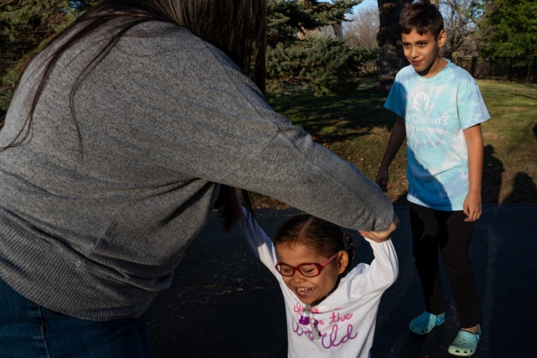 Parents of premature babies struggle to get help their children are entitled to: mom holds daughters arms in the air while playing outside with her and son