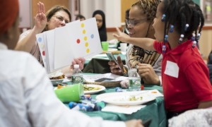 Philadelphia area parent and early caregiver support program grants: young child with beads in hair happily points to paper with colored dots at learning program