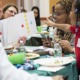 Philadelphia area parent and early caregiver support program grants: young child with beads in hair happily points to paper with colored dots at learning program