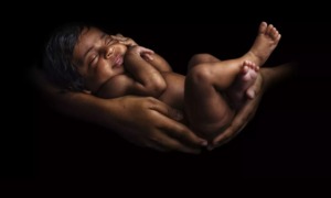 Children face unique vulnerabilities to environmental hazards at every stage of life: black infant being held by mothers arms against black background