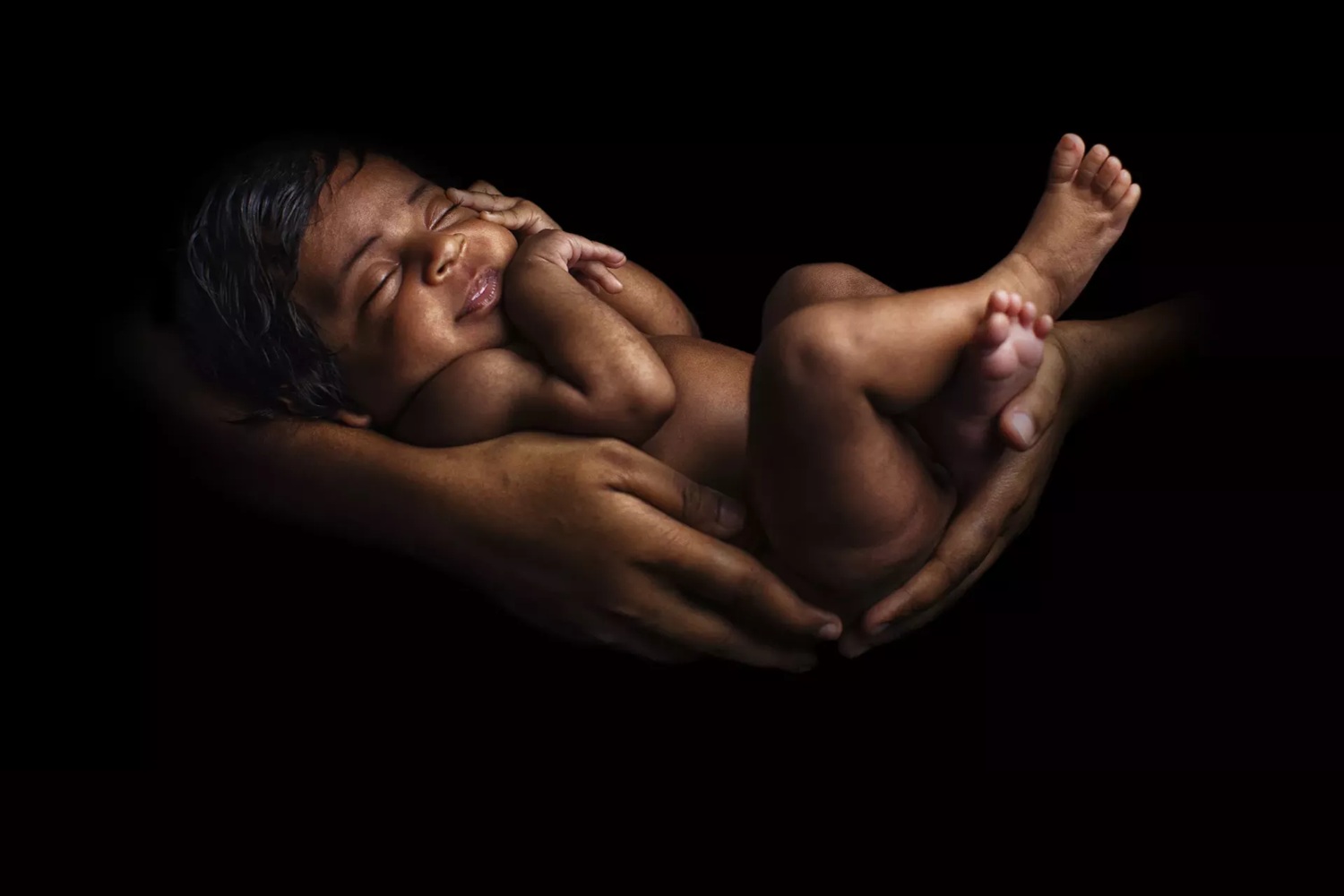 Children face unique vulnerabilities to environmental hazards at every stage of life: black infant being held by mothers arms against black background