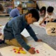 Math building blocks: Several kindergarten students sit on gray carpeted floor working with colored chips and numbered white cards