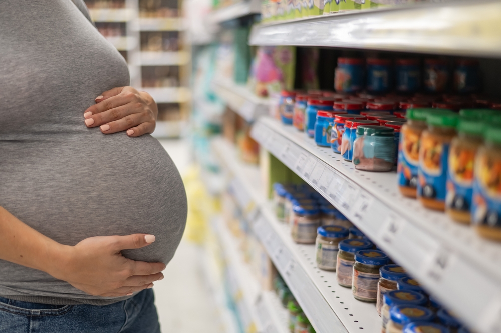 QR code baby food data: Faceless pregnant woman with hands on her stomach stands in grocery choosing baby food