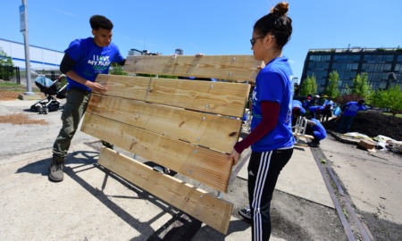 AmeriCorps cuts: two young volunteers in blue shirts move new light wood park bench into place