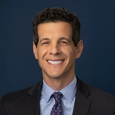 Podcast juvenile justice: Headshot man with brown hair in dark suit and light blue shirt with dark tie