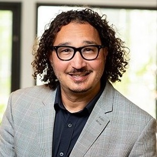 Podcast juvenile justice: Headshot man with brown hair and dark framed glasses, in light gray suit and navy blue shirt