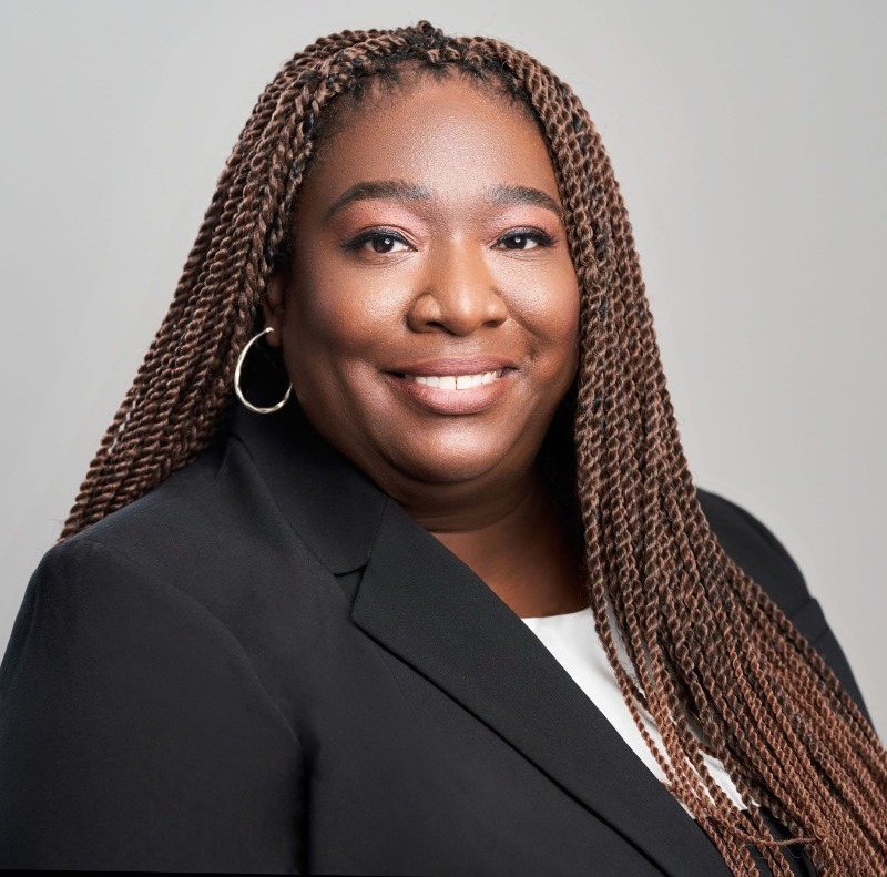 Podcast host: Black women with multiple long braids in black suit jacket with white top