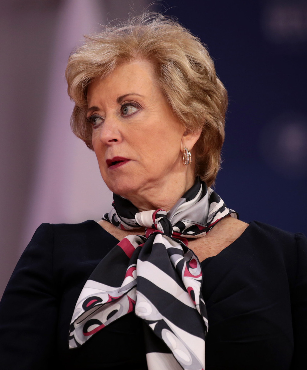 Headshot woman with short blonde hair in black top with black and white print scarf tied around neck
