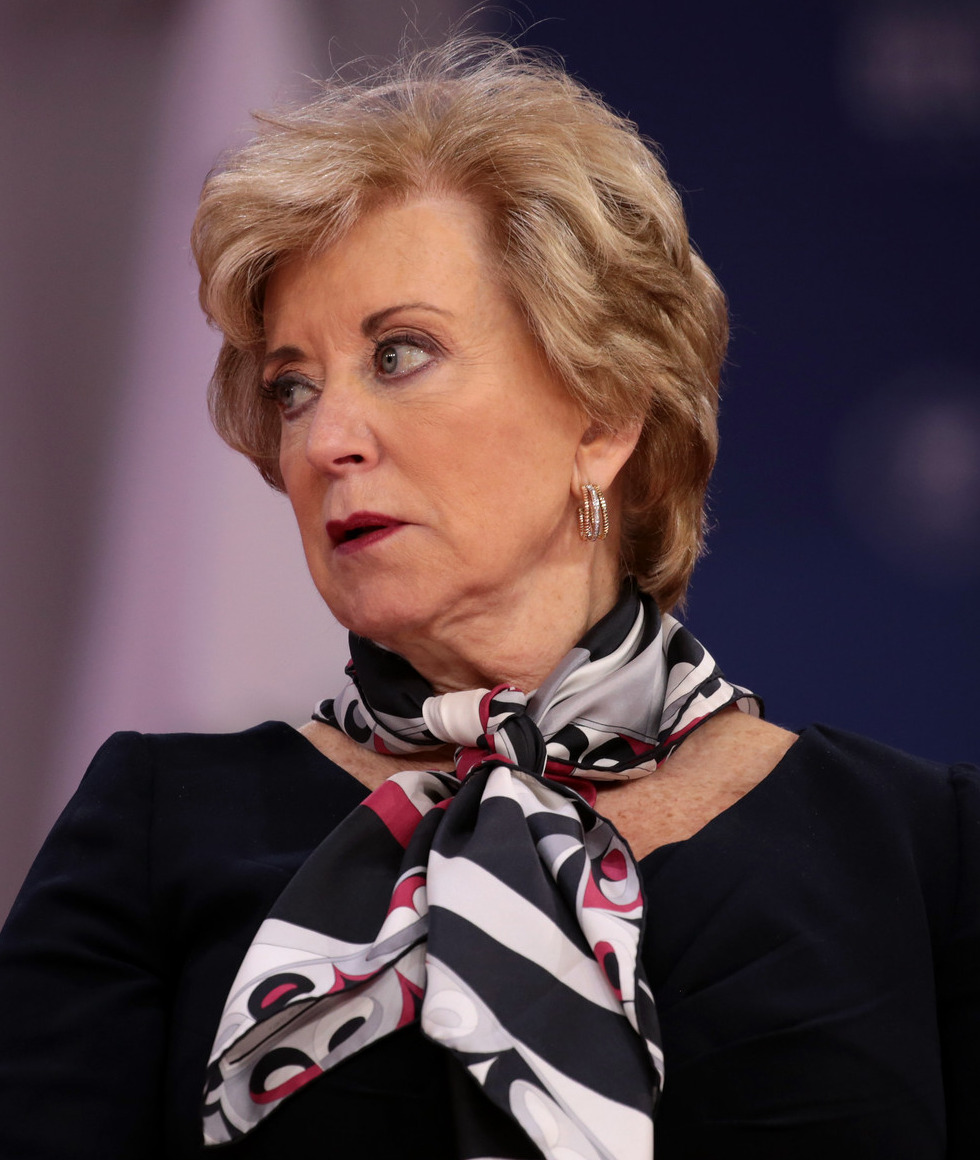 Headshot woman with short blonde hair in black top with black and white print scarf tied around neck