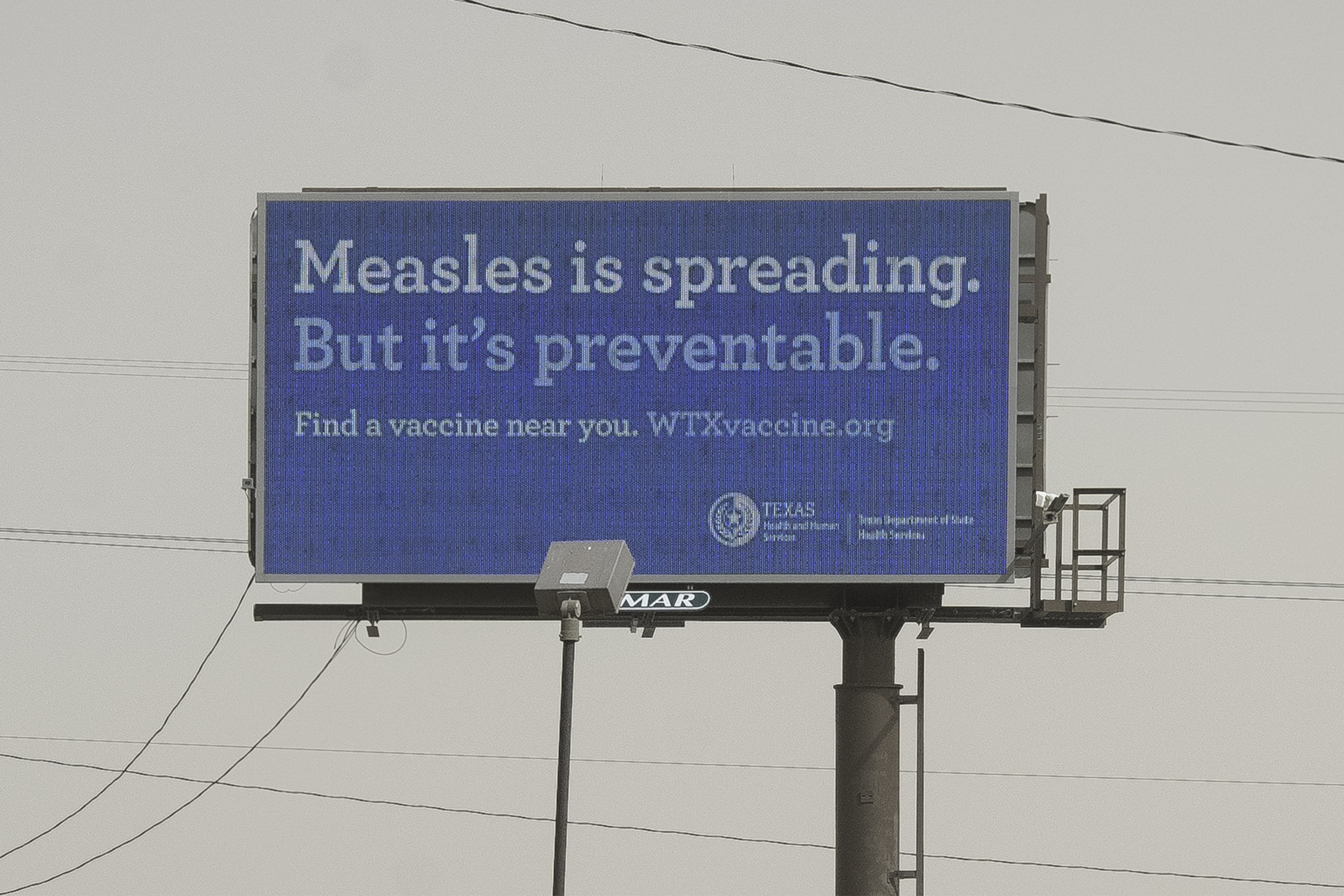 Whooping Cough & Measles outbreak: Billboard sign white text on blue background "Measles s spreading but it's preventable. Find a vaccine near you."