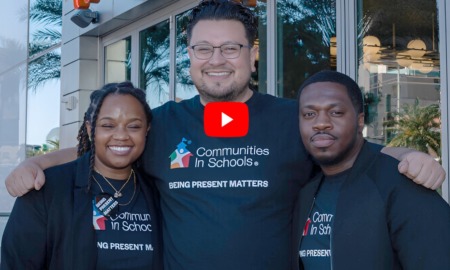 CIS and Whataburger Partnership: Three adults wearing black t-shirts with the CIS logo and Communities in Schools text stand at a double glass door entrance of modern building
