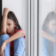 Children recovery after disaster: Sad Black preteen girl with long braids in red shirt and blue jeans sitting on windowsill.