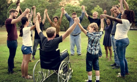 Every connections matters in education: Group of all ages people on a grass lawn surrounded by green trees standing in circle holding hands with arms raised above heads
