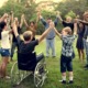 Every connections matters in education: Group of all ages people on a grass lawn surrounded by green trees standing in circle holding hands with arms raised above heads