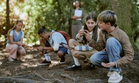 Every connections matters in youth-centered education: Group of teen boys and girls having fun picking up pine cones from ground in botanical garden during outdoor educational activity