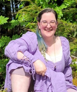 What rural students need: Blonde woman with hair pulled back sitting on grass with one knee up in loose lavender jacket and pants with white top