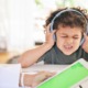 Autism Kennedy versus CDC: Young boy wearing earphones sits at table face scrunched up, eyes closed, and holding hands over ears