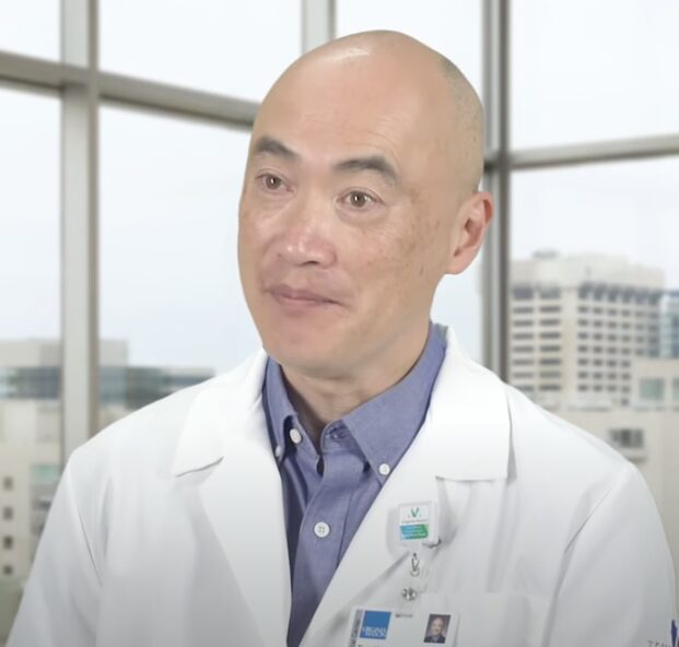 Whooping Cough & Measles outbreak: Bald Asian man in white doctor's coat and light blue shirt
