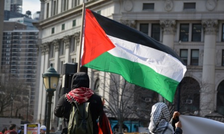 Trump is targeting international students over pro-Palestinian protests: view of protestor in hoody from behind holding Palestinian flag
