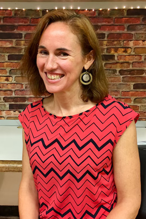 Teachers'ICE crackdown responsibilities: Seated smiling blonde woman in redand black top in front of red brick wall