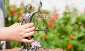 Legal counseling for behavior issues: Young child's hand holding sculpture of themis, femida or justice goddess on green leaves natural bokeh copy space background