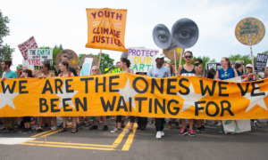 climate decision-making, Climate change: youth at street protest with many signs amd large deep yellow banner with black text, "We are the ones we've been waiting for."