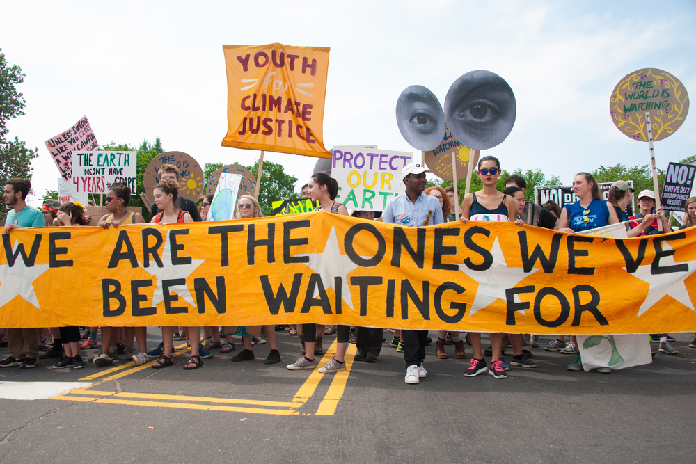 climate decision-making, Climate change: youth at street protest with many signs amd large deep yellow banner with black text, "We are the ones we've been waiting for."