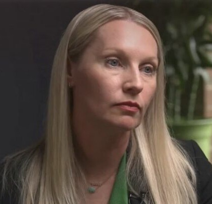 international studen visaa: Headshot woman with long blonde hair in dark jacket and kelly green blouse